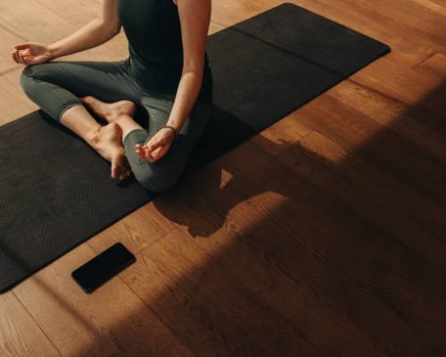 High angle view of a senior woman meditating and practicing hatha yoga. Unrecognizable woman doing a breathing exercise while sitting in easy pose. Woman following a healthy fitness routine at home.