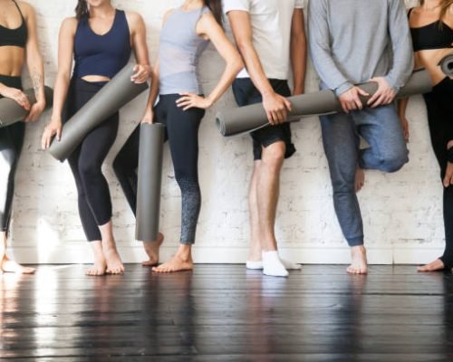 Group of young sporty people standing at wall. Students taking a rest from fitness activity, time to recover strength, waiting for a lesson to start in loft studio, close up. Healthy lifestyle concept